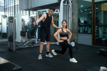 Young asian woman working out with male personal trainer in health club