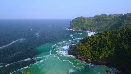 Drone view of coral hills on the edge of the sea with trees, coastal sand coral cliffs, and waves from the ocean at Sawangan Beach, Kebumen, Central Java