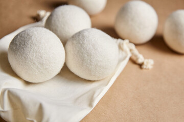 Set of white wool dryer balls resting on a cotton bag against a beige background. Eco-friendly,...