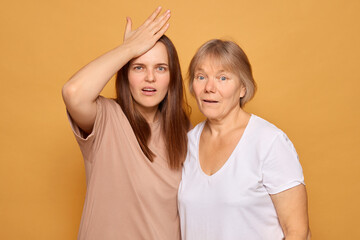 Two women stand together with surprised expressions. One woman touches her forehead while the other...
