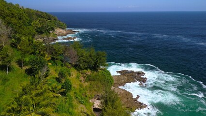 Drone view of coral hills on the edge of the sea with trees, coastal sand coral cliffs, and waves from the ocean at Sawangan Beach, Kebumen, Central Java