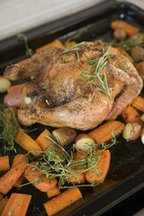 A roast chicken on a baking tray with rosemary, carrots, potatoes and sweet potatoes