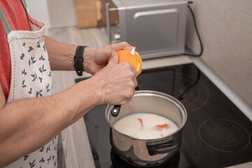 Man peeling an orange while preparing a milk-based recipe in the kitchen