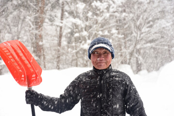 田舎で雪の降る中除雪をしている元気な老人