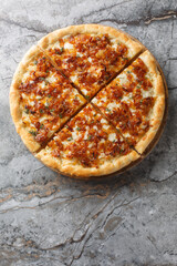 Caramelized onion pizza in French onion soup style with gruyere cheese and mozzarella close-up on wooden board on table. Vertical top view from above