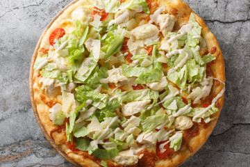 Caesar style pizza with chicken, lettuce, tomatoes, cheese and Caesar dressing closeup on the wooden board on the table. Horizontal top view from above