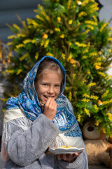 A beautiful Russian girl in a fur coat and headscarf sits on the porch of a wooden house on a sunny spring day. Family values, traditions and home comfort.Tea drinking outside the house