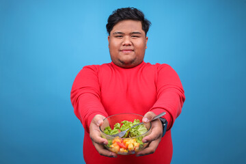 Portrait Of Fat Man Showing Salad Bowl For Diet Nutrition Over Blue Background 