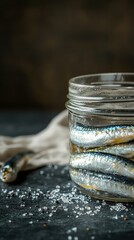 Preserved sprats in a glass jar on a dark table.