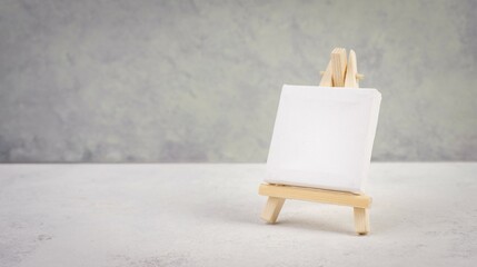 Easel with blank white canvas in front of a gray textured background, frame to add paintings and...