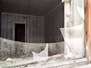 Broken window with shattered glass revealing an abandoned interior in a desolate setting