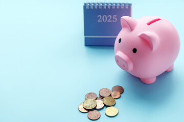 A piggy bank in the form of a pink pig, a desktop calendar for 2025 and small change coins on a blue background.