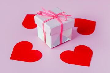 A gift box tied with a red ribbon with a bow on a pink background with red hearts. Valentine's Day gift concept.