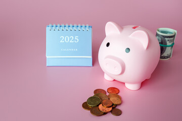 Piggy bank in form of pink pig, desktop calendar for 2025, paper banknotes in roll and exchange coins on pink background.