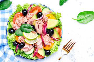 Keto salad with tuna, avocado, black olives, vegetables, lettuce and olive oil and lime dressing. White background, top view