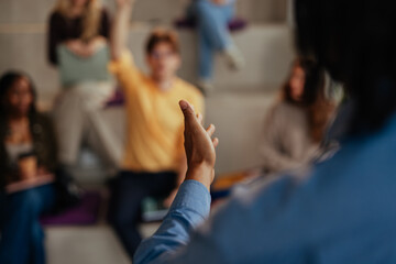Teacher gesturing while explaining lesson to students raising hands in classroom