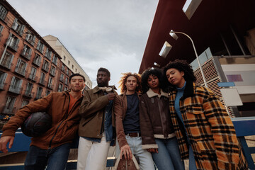 Group of young diverse friends posing in the city with basketball and skateboard