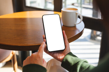Mockup image of a woman holding mobile phone with blank desktop screen in cafe