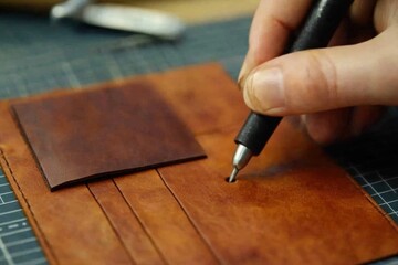 A leatherworker engraving patterns onto a wallet or bag.