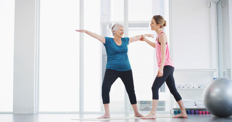 Yoga, instructor and help woman with stretching for fitness, body health or warrior pose for senior wellness. Assistance, pilates coach or exercise together for balance, physiotherapy or smile in gym
