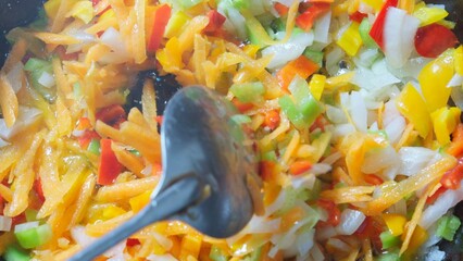 Chopped vegetables, including bell peppers of various colors and onions, are being mixed with a spoon. 