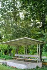 An old outdoor shelter with wooden benches surrounded by lush green trees.
