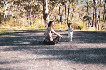 Mother and baby sit on ground in front of trees and mountain outlook