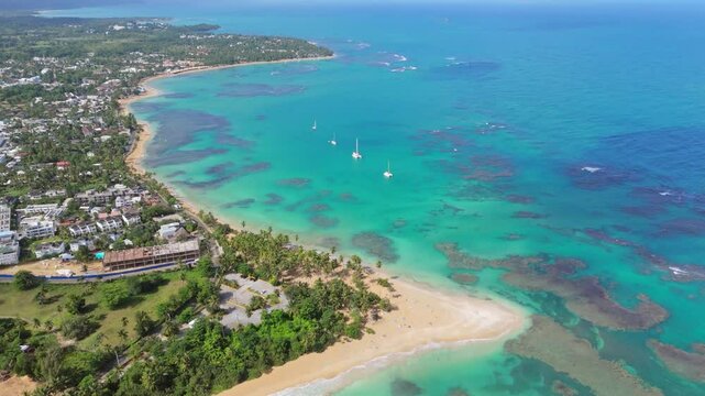 Aerial establishing shot of Punta Popy Beach in Las terrenas, Samana, Dominican Republic. Coral reef water and coastline of Dominican Republic. Sailing boat on water. Wide shot.