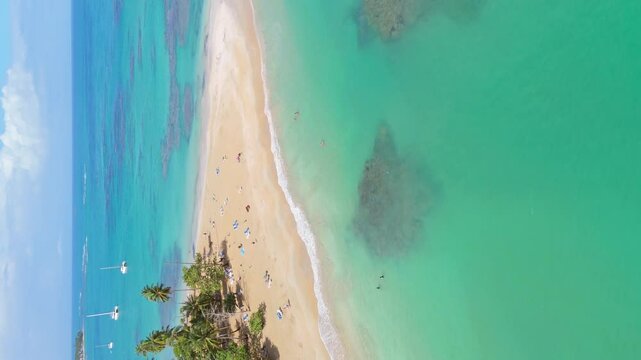 People and tourist at sandy beach of Punta Popy during sunny day. Colored landscape with clear Caribbean sea and anchored sailboats. Vertical drone orbit shot.