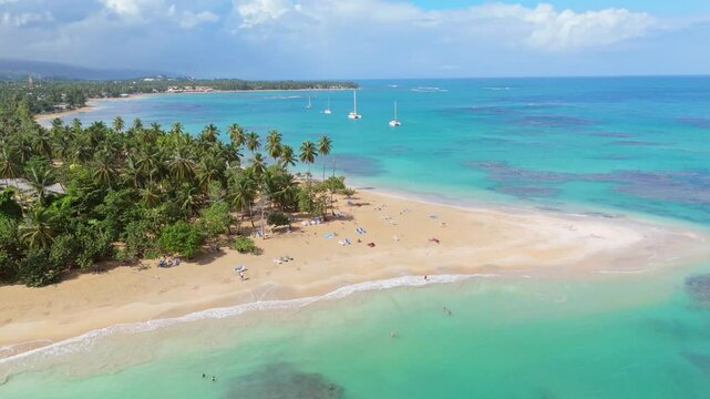 Aerial shot of Punta Popy Beach, Las Terrenas, showcasing coconut trees, turquoise waters, and anchored boats in the background, capturing the natural beauty of the Caribbean