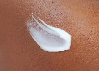 Close-up of smooth brown skin with a swipe of white moisturizing cream applied for hydration and care. Dermatology cosmetics product