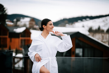 Woman in white robe enjoying winter mountains during holiday getaway with snow-capped peaks...