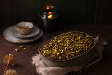 Dubai chocolate tiramisu with pistachio and chocolate ganache on a dark background, candle. Italian tiramisu dessert with layers of lady finger biscuit and mascarpone. Professional food photography. 