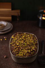 Dubai chocolate tiramisu with pistachio and chocolate ganache on a dark background, candle. Italian tiramisu dessert with layers of lady finger biscuit and mascarpone. Professional food photography. 