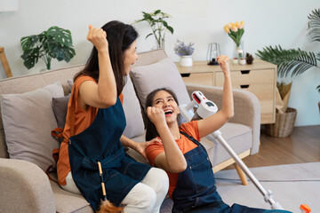 Two women celebrating their cleaning achievements while sitting on a couch, one with a vacuum...