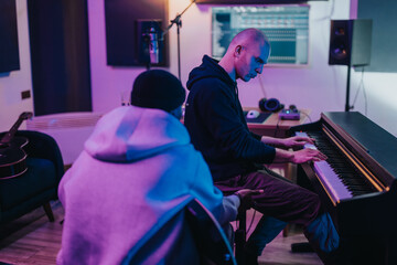 Two diverse musicians engaged in creating music, with one playing the keyboard. The studio has a modern, artistic atmosphere, featuring musical instruments and recording equipment.