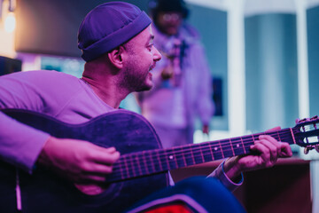 A joyful scene of multiracial musicians jamming together in a neon-lit recording studio. The image captures creativity, collaboration, and the joy of making music with diverse artists playing guitar