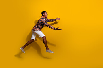 Young man in stylish printed shirt and white shorts posing energetically against vibrant yellow background