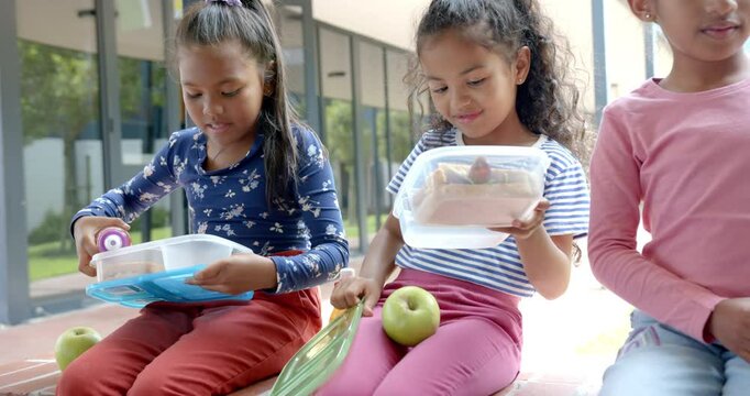 In school, three children sitting with lunchboxes and apple during break