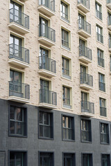 Contemporary building facade featuring small balconies and a mix of brick and dark panels. Urban housing concept on a clear day