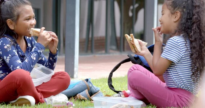 In school, two biracial young girls are enjoying lunch outside