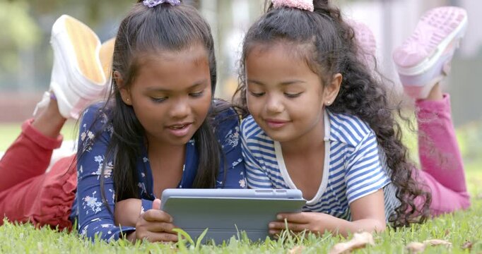 Lying on grass, two girls using tablet together, enjoying outdoor activity