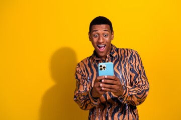 Excited young man with a smartphone in a colorful shirt against a vibrant yellow backdrop