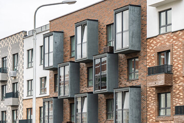 Contemporary apartment facade with multicolored brick walls, windows, and protruding gray balconies. Urban housing concept