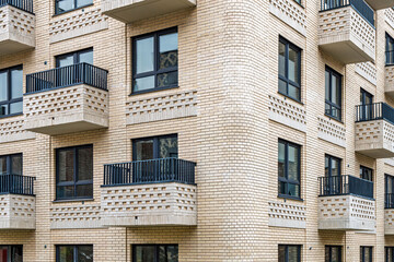 Modern beige brick building with multiple balconies with metal railings and windows, concept of urban architecture