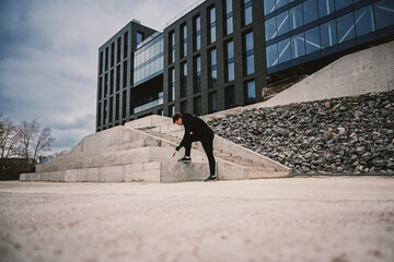 A teenager warms up before playing sports in the midst of modern urban architecture.