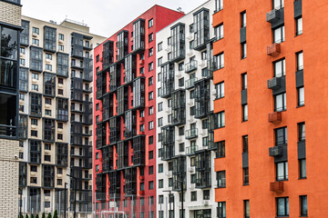 Fototapeta premium Contemporary apartment buildings with orange, white, and red facades, featuring numerous balconies with dark-framed windows. Urban housing concept