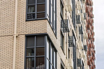 Contemporary multi-story buildings with beige, red brick and glass facades, with dark-framed balconies and windows, low angle view