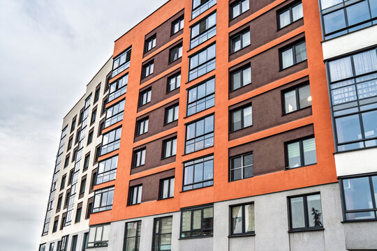 Modern apartment building facade, featuring beige, orange, and brown tones, with dark-framed windows, low angle view. Urban housing concept