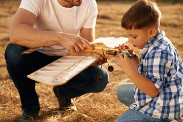 Messing around with broken toy. Father and son are with wooden plane on the field